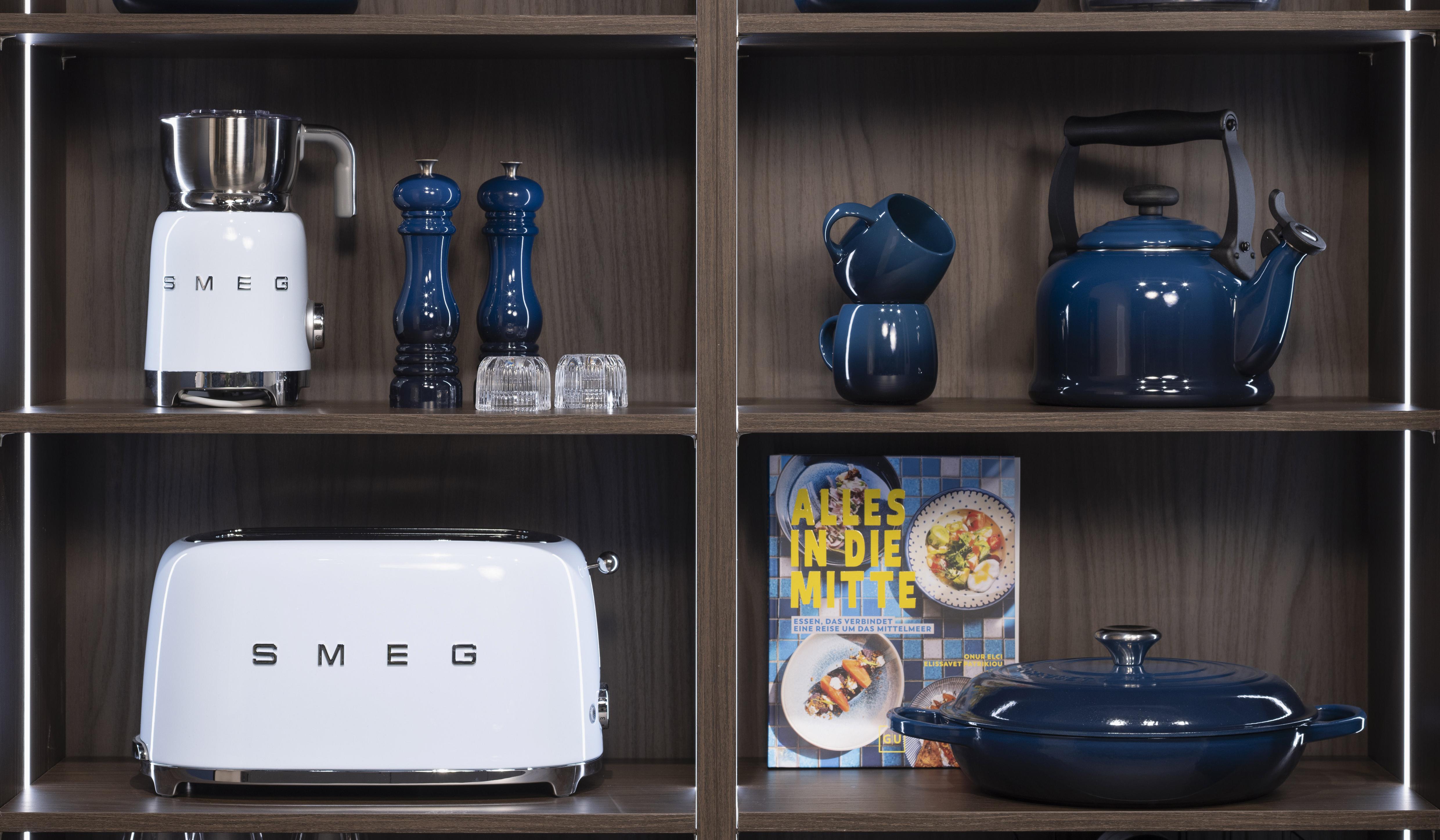 Küchenregal mit blauem Geschirr, weißem Toaster und Wasserkocher, Kochbuch in der Mitte.