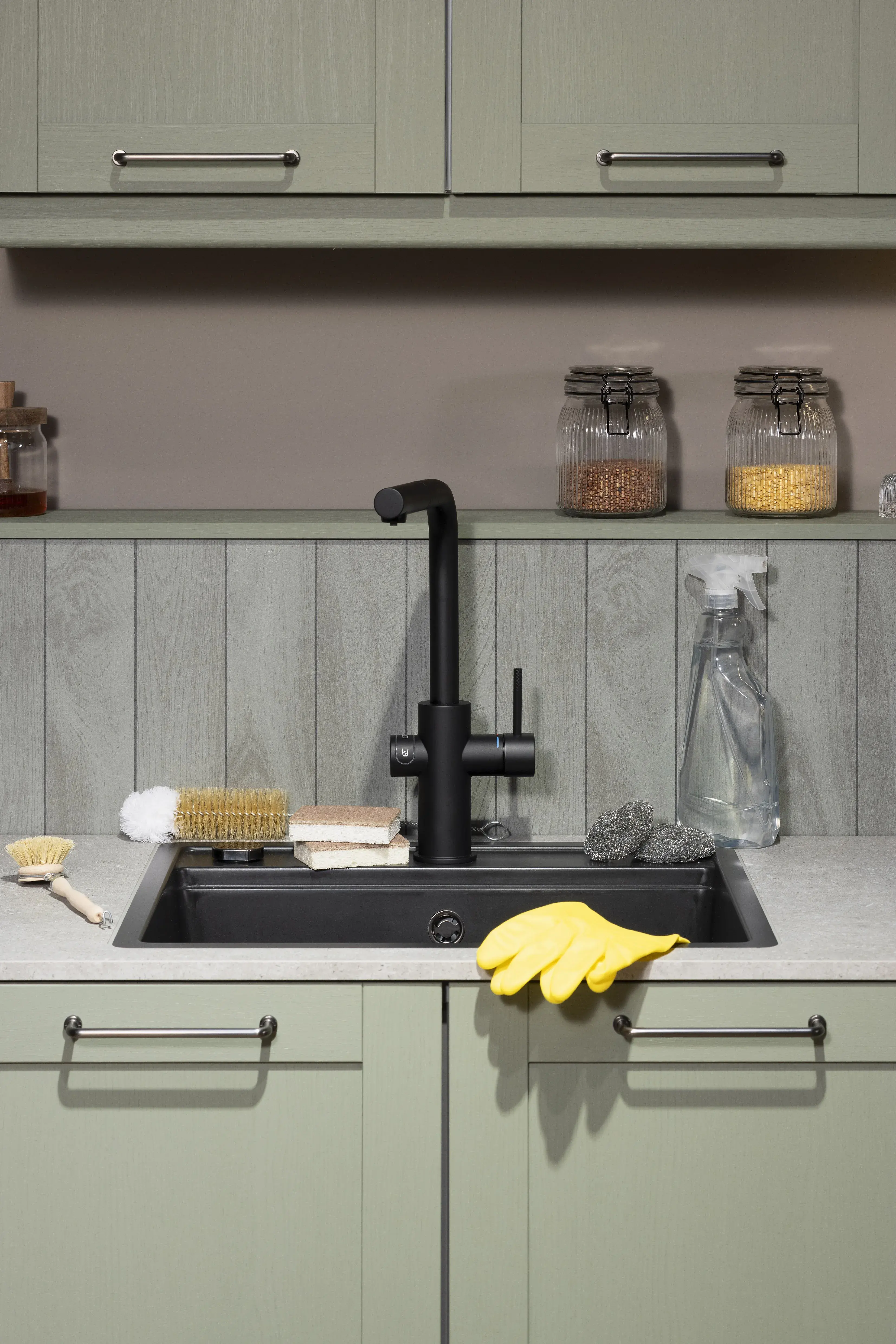Moderne Küchenspüle mit gelbem Handschuh, Schwamm, Bürste und Vorratsgläsern im Hintergrund.