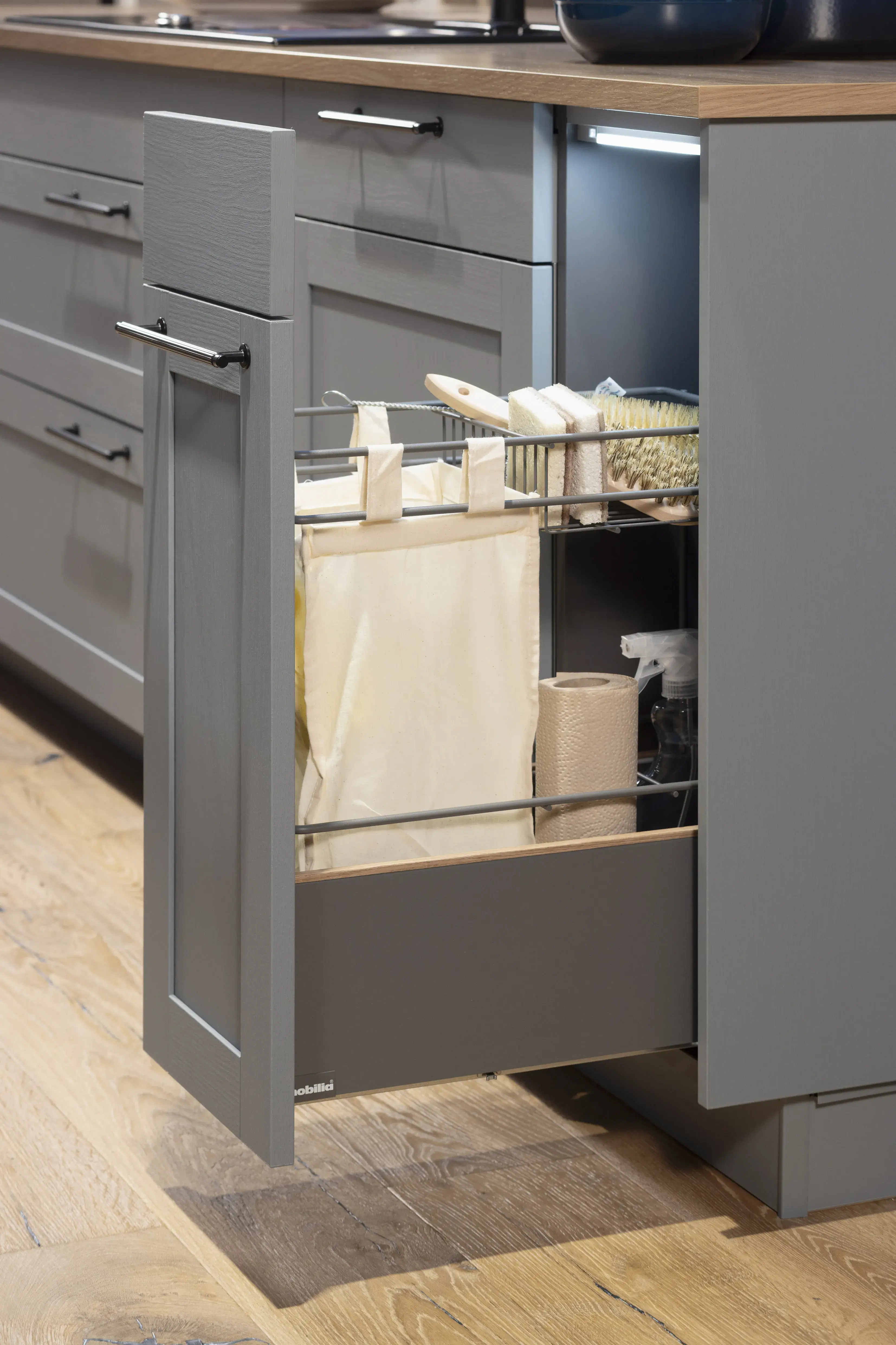 Grau Schrank mit ausziehbarer Schublade und Reinigungsmitteln in moderner Küche.
